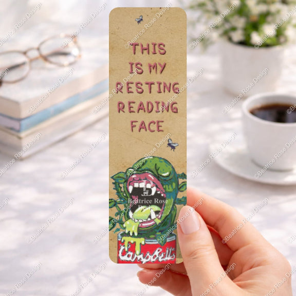 Bookmark with a cartoon character and text held by a hand on a desk with books and coffee.