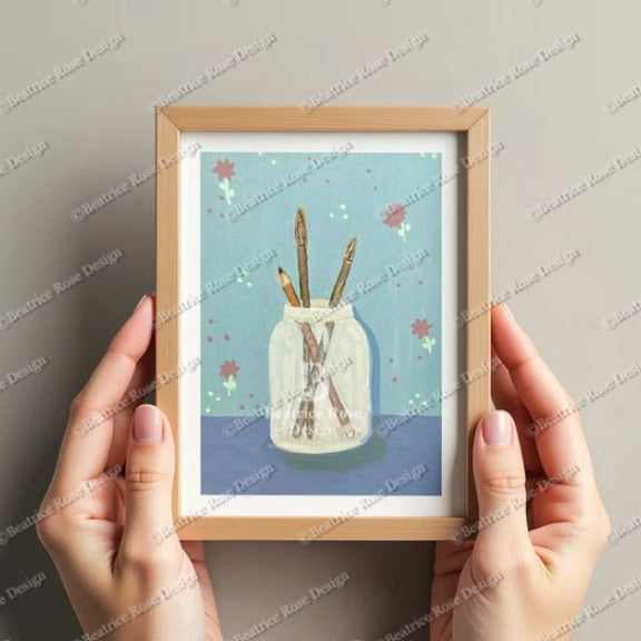 Framed artwork of a jar with sticks on a blue background held by hands against a gray wall.