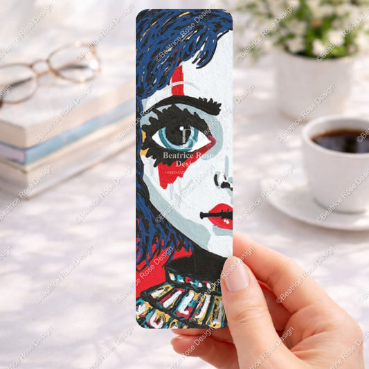Bookmark with artistic design held by a hand on a desk with coffee and books.