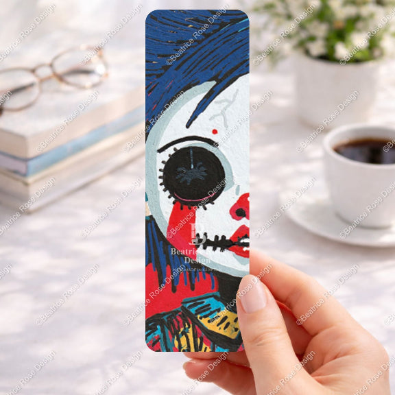 Bookmark with artistic design held by a hand on a desk with coffee and books.