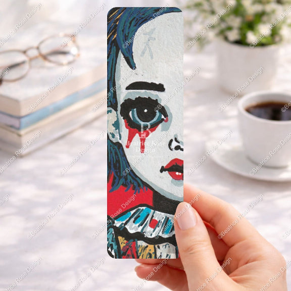 Bookmark with artistic design held by a hand on a desk with coffee and books.