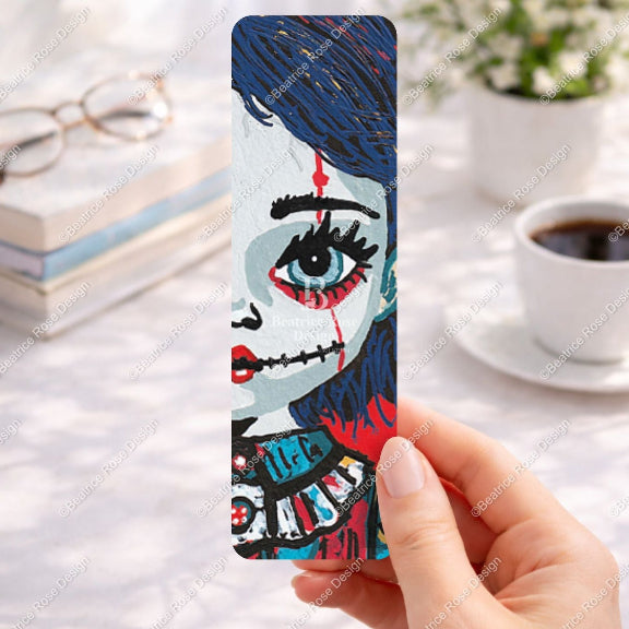 Bookmark with artistic design held by a hand on a desk with books and coffee.