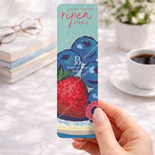 Hand holding a card with berries design on a blurred background of books and coffee.