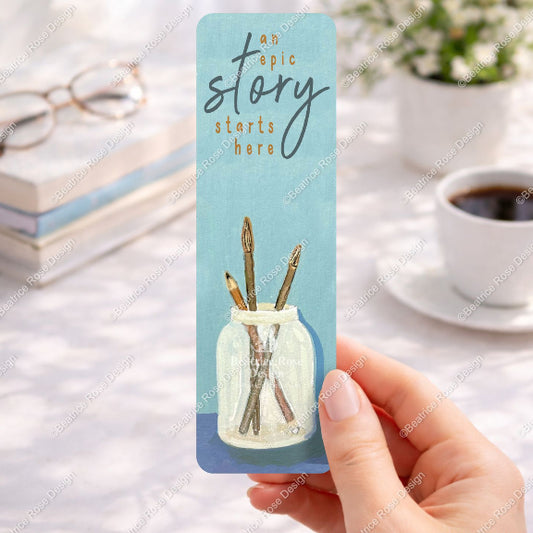 Bookmark with a jar of pencils and 'an epic story starts here' text, held by a hand on a blurred desk background.