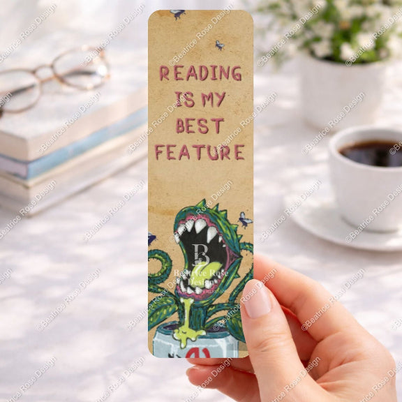 Bookmark with 'Reading is my best feature' text held by a hand on a desk with books and coffee.