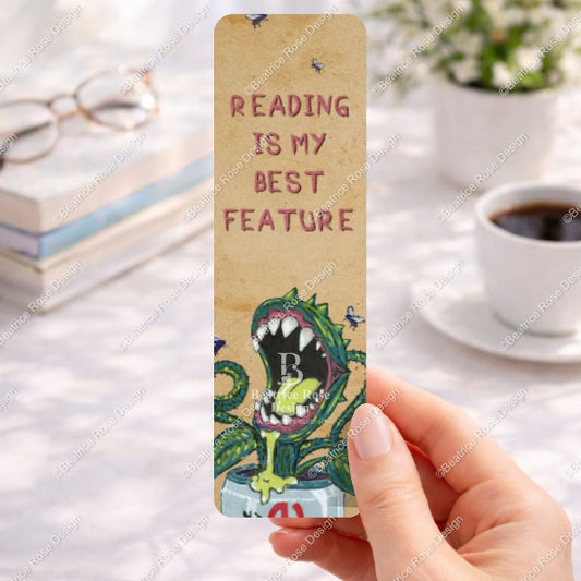 Bookmark with 'Reading is my best feature' text held by a hand on a desk with books and coffee.