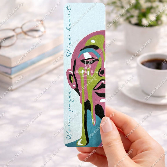 Colorful bookmark held by a hand with a blurred background of a desk with a cup of coffee and glasses.