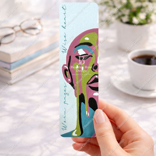 Colorful bookmark held by a hand with a blurred background of a desk with a cup of coffee and glasses.