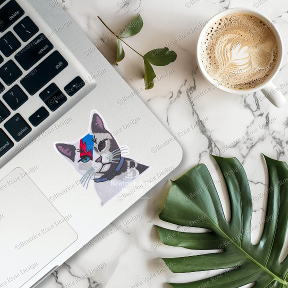 Laptop with a cat sticker, coffee cup, and leaf on a marble surface
