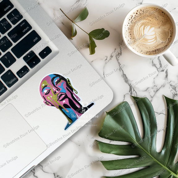 Laptop with a colorful sticker on a marble surface with a coffee cup and leaf.