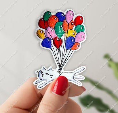 Sticker of a cat with colorful balloons held by a hand with red nail polish.