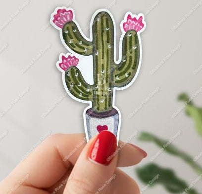Hand holding a cactus-shaped sticker with pink flowers on a light gray background