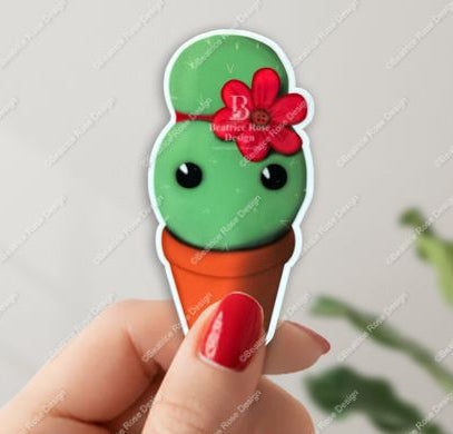 Hand holding a cactus-shaped ice sticker cone with a red bow against a light gray background.