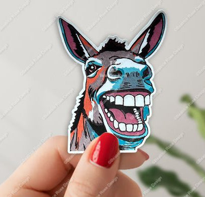 Hand holding a colorful sticker of a donkey's face against a light gray background