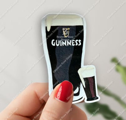 Sticker of a pint of Guinness held by a hand with red nail polish on a light gray background.