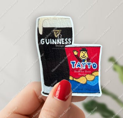 Two miniature beer bottles, one Guinness and one Tayto, held between fingers against a light background.