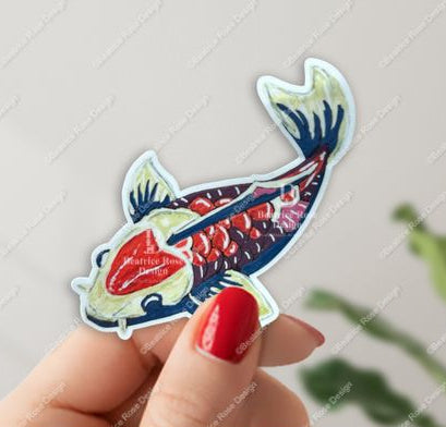 Hand holding a colorful fish-shaped sticker with a blurred background
